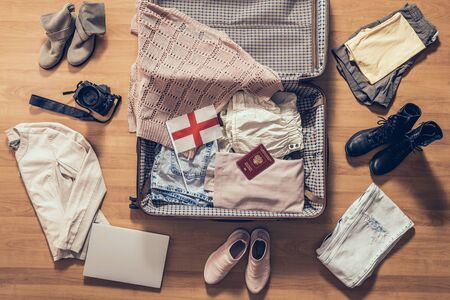 Woman's clothes, laptop, camera, russian passport and flag of England lying on the parquet floor near and in the open suitcase. Travel conceptの写真素材