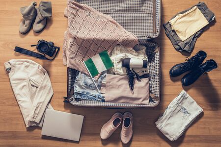 Woman's clothes, laptop, camera and flag of Nigeria lying on the parquet floor near and in the open suitcase. Travel conceptの写真素材