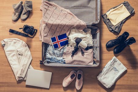 Woman's clothes, laptop, camera and flag of Iceland lying on the parquet floor near and in the open suitcase. Travel conceptの写真素材