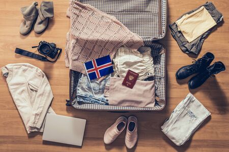 Woman's clothes, laptop, camera, russian passport and flag of Iceland lying on the parquet floor near and in the open suitcase. Travel conceptの写真素材