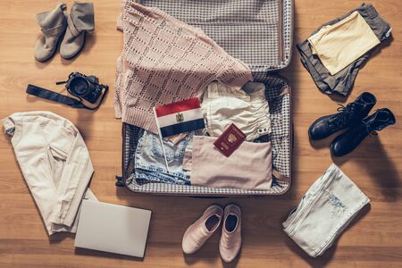 Woman's clothes, laptop, camera, russian passport and flag of Egypt lying on the parquet floor near and in the open suitcase. Travel conceptの写真素材