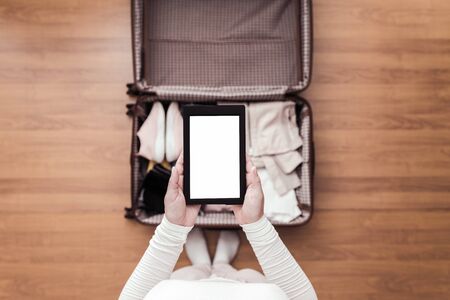 Top view of woman packing a luggage for a new journey. Female standing above suitcase with electronic note pad and cup of coffee. Space for text.の写真素材