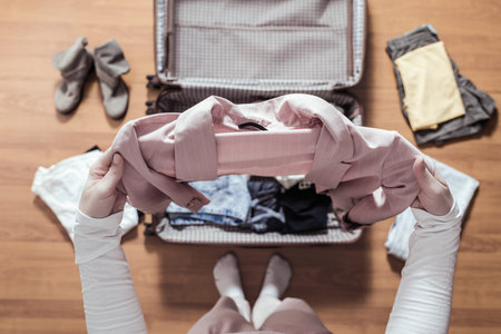 Top view of woman hands packing a pink blazer in a luggage (suitcase) for a new journey.