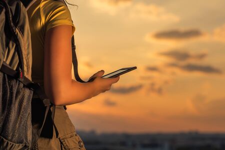 woman hiker in shorts and a t-shirt with a backpack  and the tablet on a sunset backgroundの写真素材