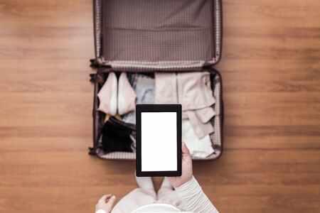 Top view of woman packing a luggage for a new journey. Female standing above suitcase with electronic note pad and cup of coffee. Space for text.の写真素材