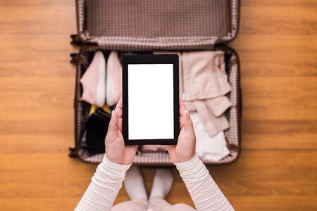 Top view of woman packing a luggage for a new journey. Female standing above suitcase with electronic note pad and cup of coffee. Space for text.の写真素材