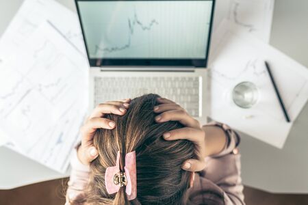 Top view. Tired business woman with headache at office with glass of water and pill on the background of graphics and charts printed on the paper.の写真素材