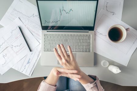 Top view.  business woman sitting at table and applying hand cream  working on the laptop with graphics and charts printed on the paper.の写真素材