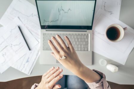 Top view.  business woman sitting at table and applying hand cream  working on the laptop with graphics and charts printed on the paper.の写真素材