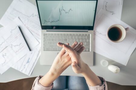 Top view.  business woman sitting at table and applying hand cream  working on the laptop with graphics and charts printed on the paper.の写真素材