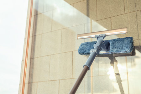 Girl Cleaning open Window of balcony by spraying Cleaning Products and wiping with mop Sponge at the...