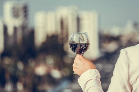 Woman hand with glass of red wine against the city background at summer eveningの写真素材