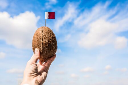 Tropical coconut with Qatar flag in the form of a toothpick in female hands.  Travel conceptの写真素材