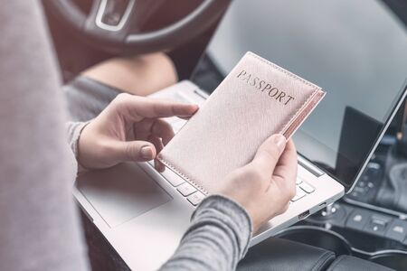 Woman in the car with laptop and passport in a pink cover. Travel concept.の写真素材