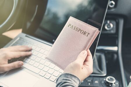 Woman in the car with laptop and passport in a pink cover. Travel concept.の写真素材