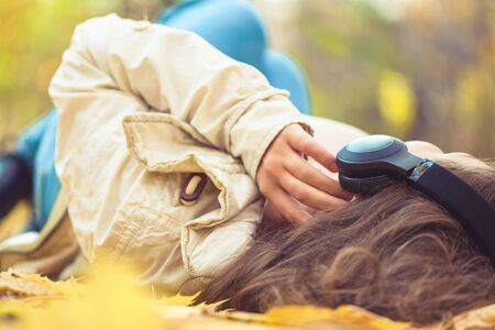 young woman in the headphones listening music lying on the ground of an autumn forest with colorful maple leaves. Indian summer seasonの写真素材