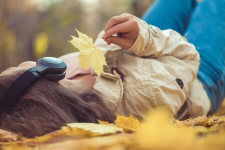 young woman in the headphones listening music lying on the ground of an autumn forest with colorful maple leaves. Indian summer seasonの写真素材