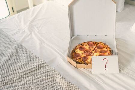 Open box of pizza on the big bed and card with question mark. Conceptの写真素材