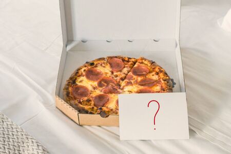 Open box of pizza on the big bed and card with question mark. Conceptの写真素材