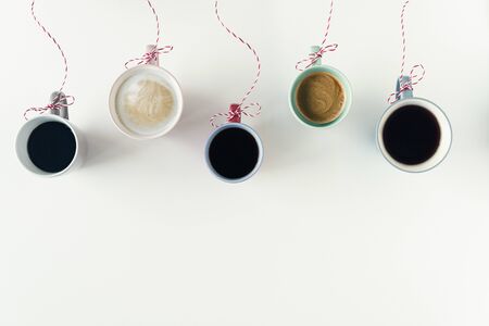 Winter garland with Christmas toy made from cups of coffee hanging on a red white string or twine tied in a bow. White table. Winter Concept. Creativeの写真素材