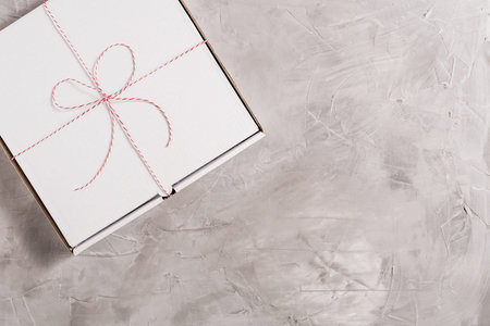 Closed box of pizza tied of christmas red white string or twine in a bow on the on grey concrete...
