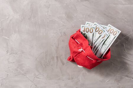 Bundle of US hundred dollars in the funny santa claus red bag from felt on the gray concrete background. Cristmas Concept.の写真素材