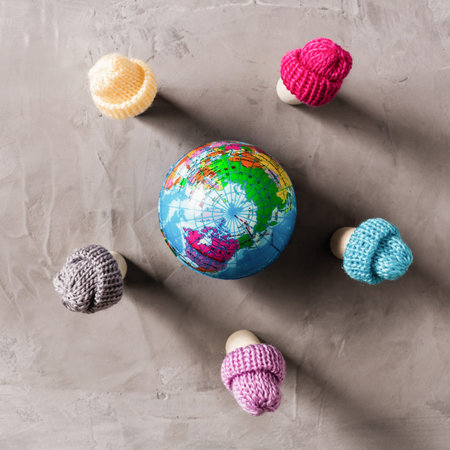 wooden people in the knitted hats standing around small rubber earth globe on the gray asphalt in the snow. Concept.の写真素材
