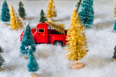Creative Christmas decoration with red truck and colorful snowy spruces in the snow. Winter forest....