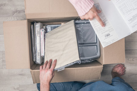 Couple man and woman shopper sitting on floor at home opening carton box and checking stationery...