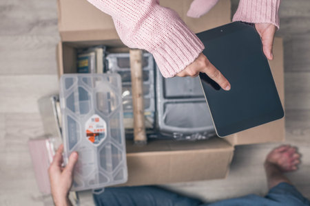 Couple man and woman shopper using tablet checking order sitting on floor at home and opening carton...