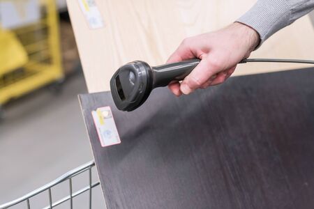 Man with manual scanner of barcodes scans and buying plywood, mdf lying in a shopping cart in a hardware store. self catering の写真素材