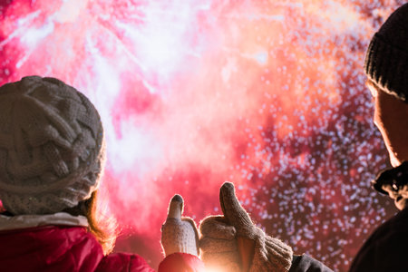Merry man and woman in the winter clothes during fireworks at night.