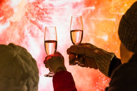 Merry man and woman in the winter clothes toasting with glasses champagne celebrate holiday christmas or new year during fireworks at night.の写真素材