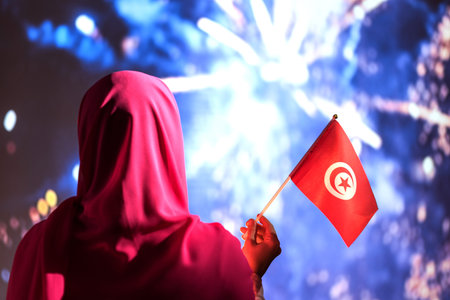 Muslim woman in a scarf holding flag of Tunisia during fireworks at night.の写真素材