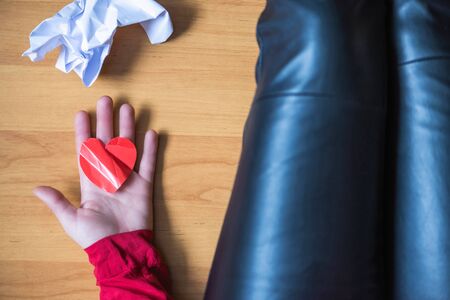 woman with crumpled paper heart in the hand sitting on the floor.  Broken relationships in bad Valentine's day. concept. Top viewの写真素材