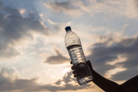 Girl holding in the hand a plastic bottle with crystal clear mineral water opposite the rays of the sunset sky. Conceptの写真素材