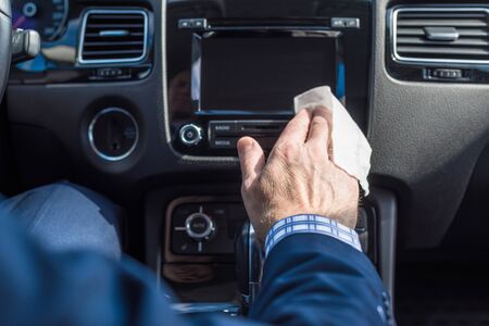Man in a blue suit cleaning front dashboard of a car by a  wet napkin. の写真素材