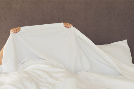 A young woman covers herself with the sheets and hides. Nightmares, insomnia, phobias, panic...