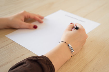 Student girl hand with bracelet and love word. Empty examination paper sheet on the table. First...