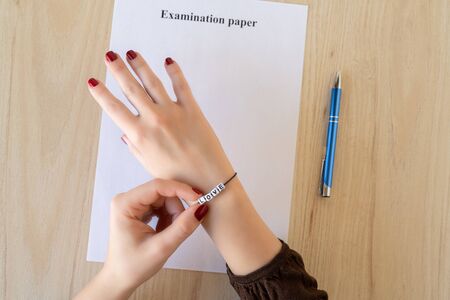 Student girl hand with bracelet and love word. Empty examination paper sheet on the table. First love during university exam. Conceptの写真素材