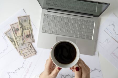 Woman freelancer holding pack of banknotes fifty U.S. dollars in hand and counting profit, income. laptop with graphics and charts printed on the paper on office table. Forex exchange. Flat layの写真素材