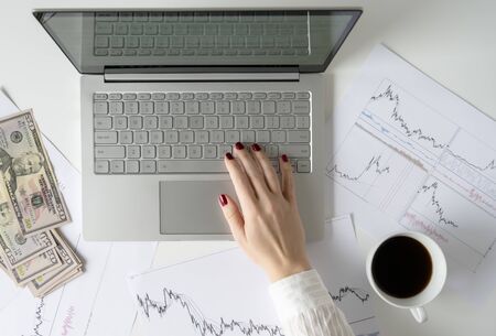 Woman freelancer holding pack of banknotes fifty U.S. dollars in hand and counting profit, income. laptop with graphics and charts printed on the paper on office table. Forex exchange. Flat layの写真素材