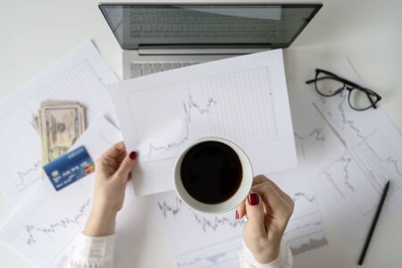 Woman freelancer with banknotes fifty U.S. dollars and credit card. counting profit, income. laptop, graphics and charts printed on the paper on office table. Forex exchange. Flat layの写真素材