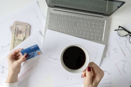 Woman freelancer with banknotes fifty U.S. dollars and credit card. counting profit, income. laptop, graphics and charts printed on the paper on office table. Forex exchange. Flat layの写真素材