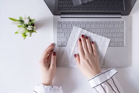 A woman worker cleaning with antivirus wet wipe a laptop and a working office desk before starting work for protect herself from bacteria and virus.の写真素材