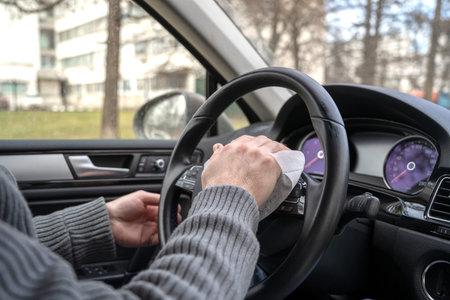 Man cleaning steering wheel of a car using antivirus antibacterial wet wipe (napkin) for protect...