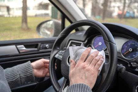 Man cleaning steering wheel of a car using antivirus antibacterial wet wipe (napkin) for protect...