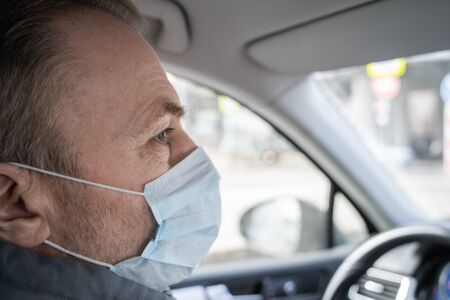 face of middle aged man in the medical mask for protect himself from bacteria and virus driving a car. Coronavirus. Pandemicの写真素材
