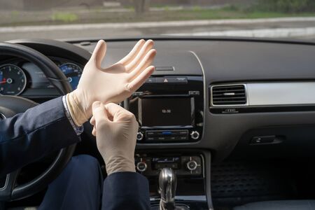 Middle age businessman in blue suit puts on rubber gloves for protect himself from bacteria and virus while driving a car. Coronavirus. Pandemicの写真素材
