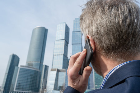 Alone middle-aged gray-haired businessman in a blue suit calling by phone standing opposite Moscow...